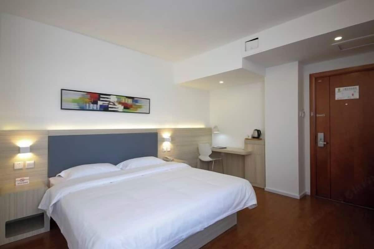 A hotel room with a bed, bedside lamps, a desk, and a door.