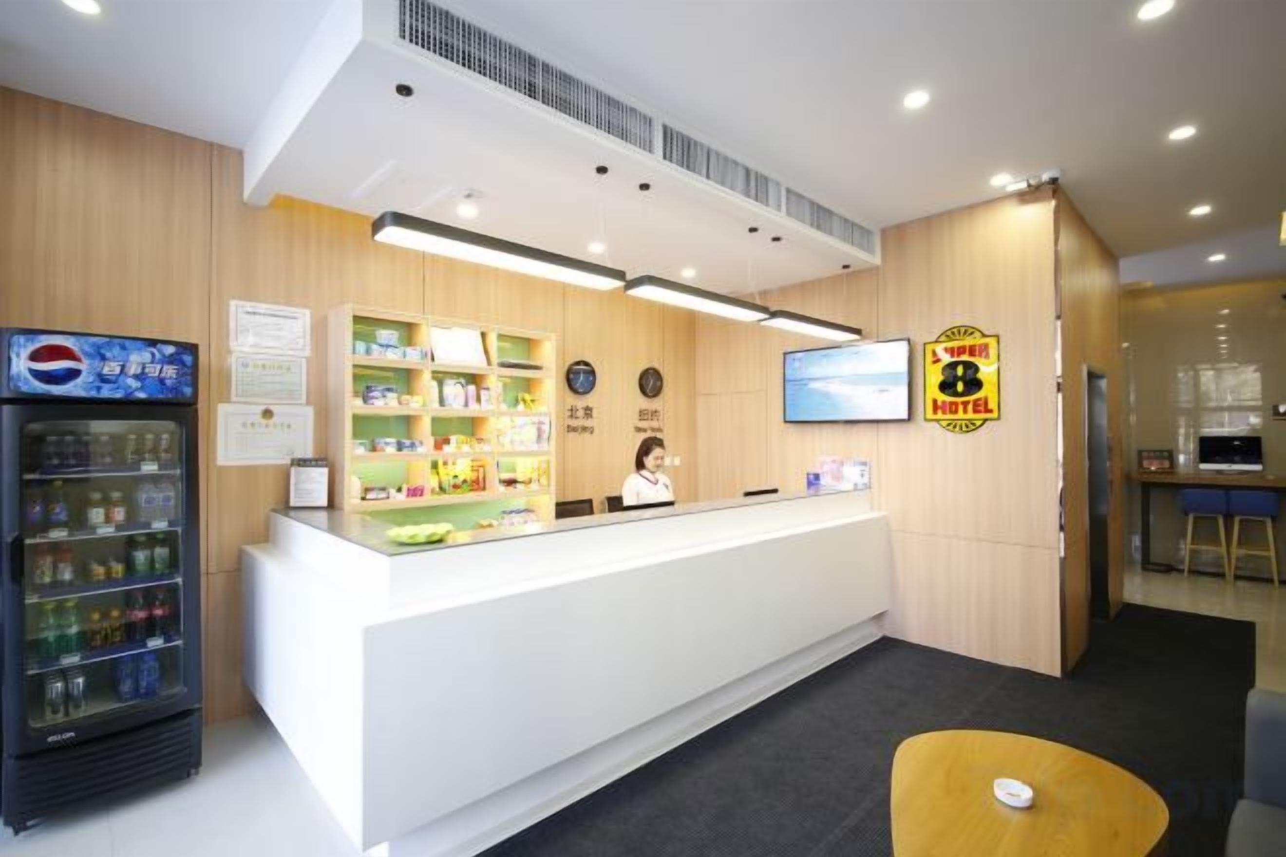 Zona de recepción de un hotel con mostrador, refrigerador y pantalla de televisión.