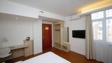 A hotel room with a bed, a desk with a chair, a TV, a wardrobe, and a window with curtains.