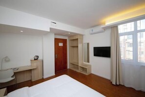 Ein Hotelzimmer mit Bett, Schreibtisch mit Stuhl, Fernseher, Kleiderschrank und einem Fenster mit Vorhängen.