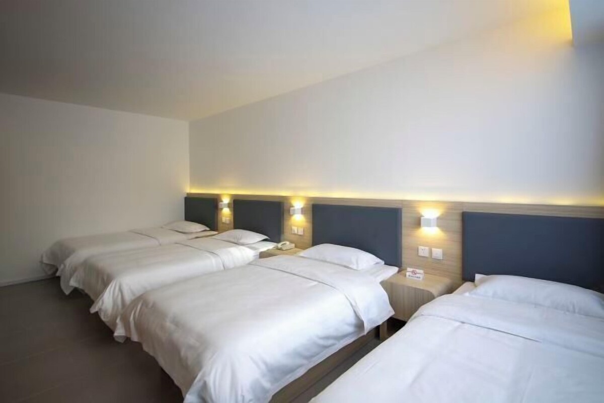 Ein Hotelzimmer mit drei Betten, jeweils mit Kopfteil und Nachttischlampen.
