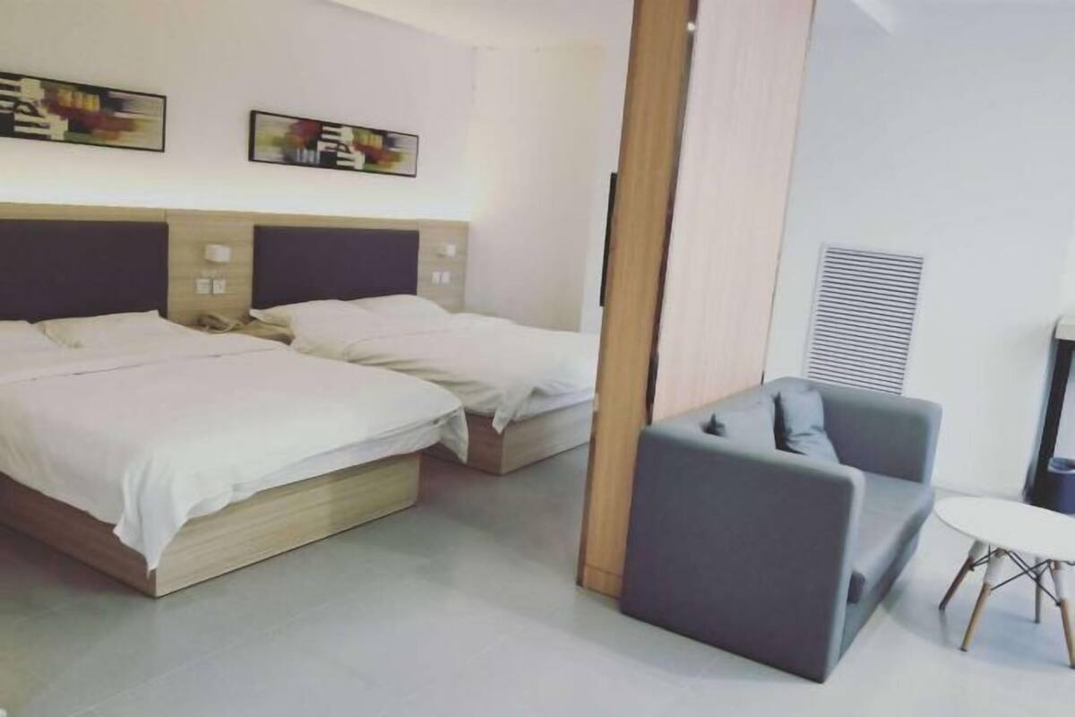 A hotel room with two beds, a grey sofa, a small table, and artwork on the wall.