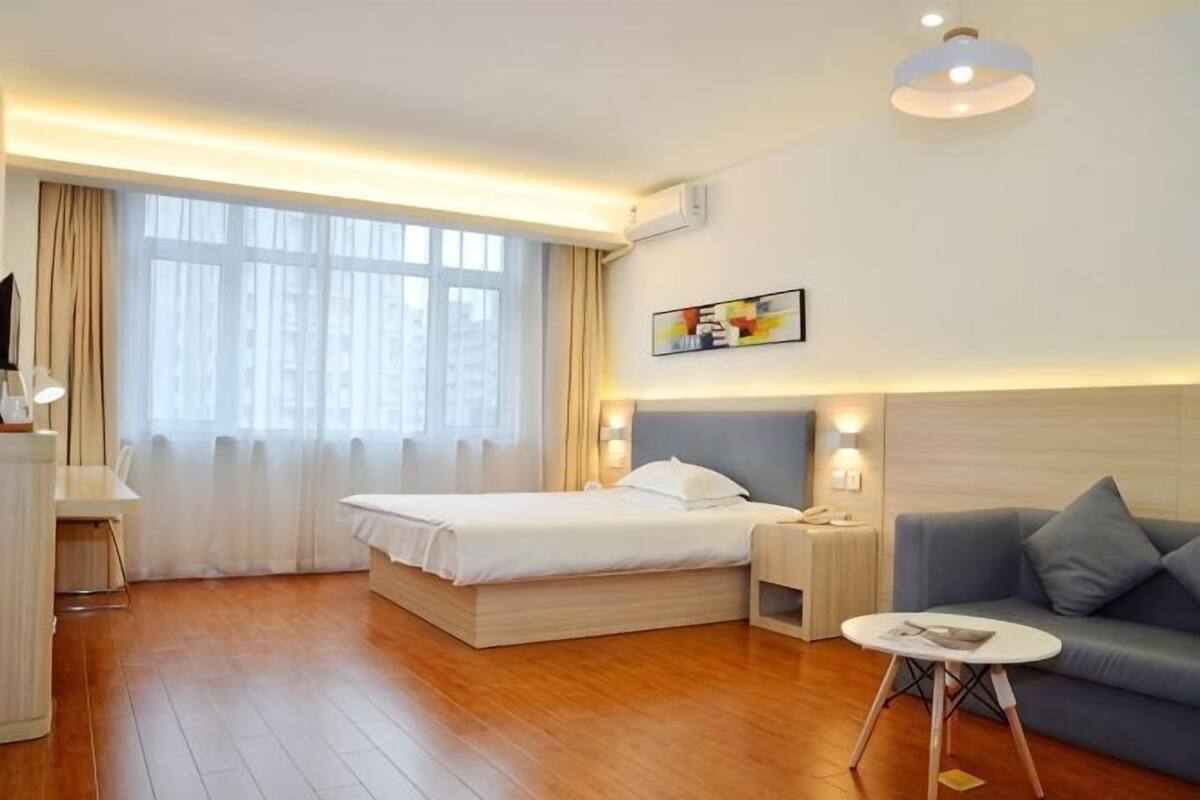 A hotel room with a bed, a sofa, a small table, and a painting on the wall.