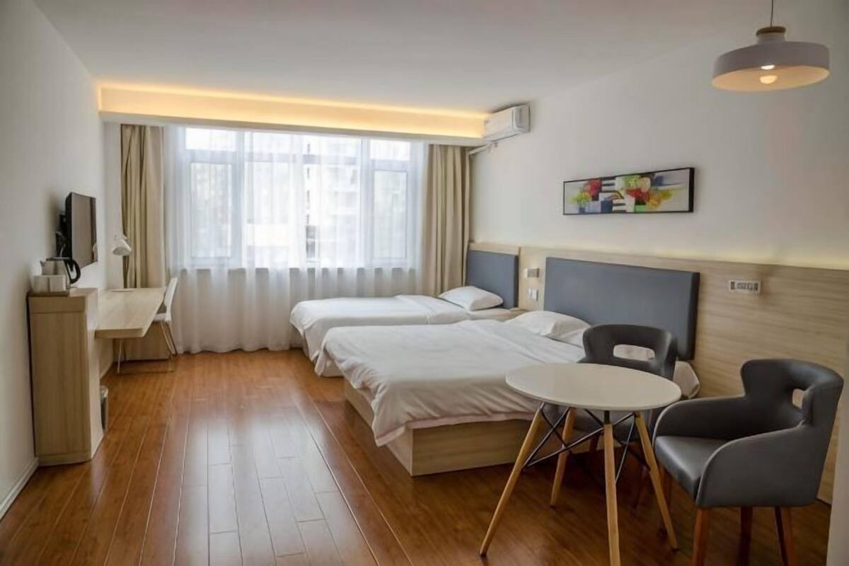 A hotel room with two beds, a desk, a chair, a small table, and a window with curtains.