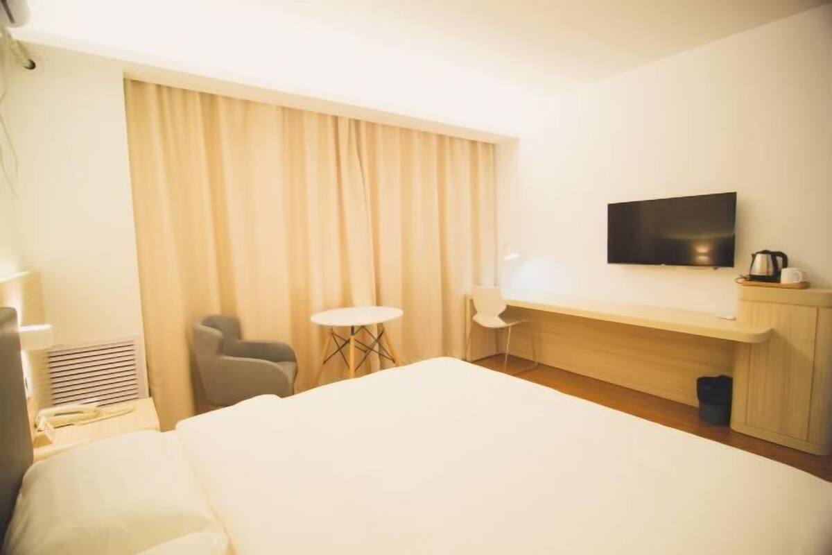 A hotel room with a bed, a desk, a chair, a television, and a window with curtains.