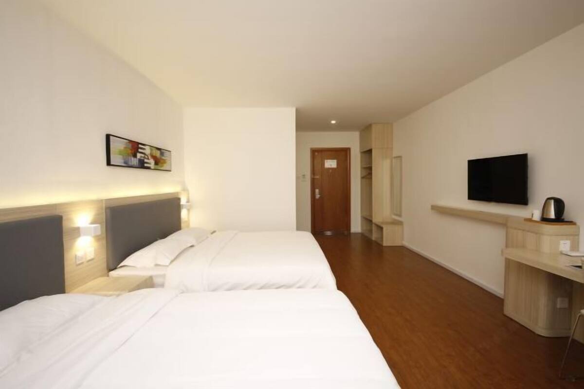 A hotel room with two beds, a TV, a desk, and a door in the background.
