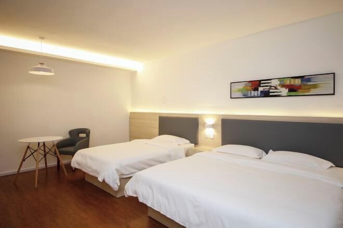 Ein Hotelzimmer mit zwei Einzelbetten, einem kleinen Tisch, einem Sessel und einer Wandleuchte.