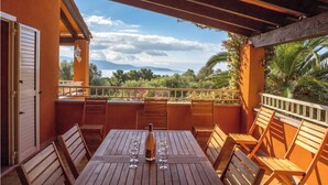 An outdoor patio with a wooden table set for two, a bottle of wine, and several glasses. The patio overlooks a lush landscape with trees and a distant mountain range. - 10 people sea view villa with pool in the south part of Corsica (Olmeto, Abbartelo)