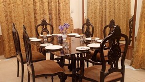 Uma sala de jantar com uma mesa redonda posta para seis pessoas, rodeada por cadeiras ornamentadas com assentos acolchoados.