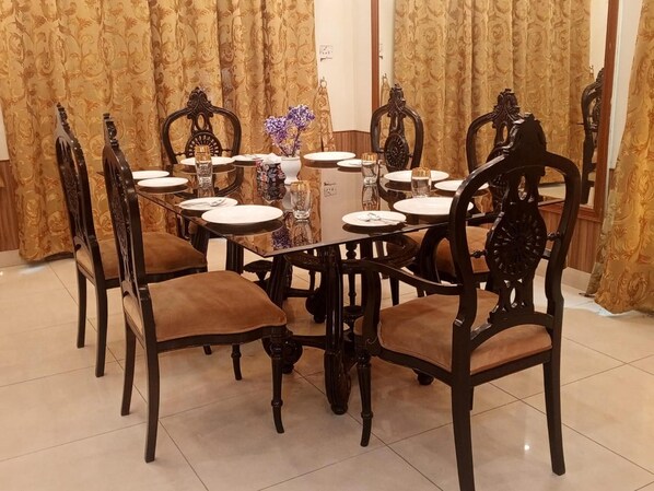 A dining area with a round table set for six, surrounded by ornate chairs with cushioned seats.