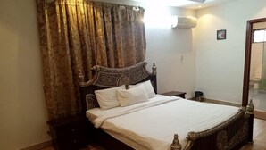 Quarto com cama grande, cabeceira decorada e cortinas.
