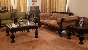 Uma sala de estar tradicional com uma poltrona verde, um sofá estampado e uma mesa de centro de vidro.
