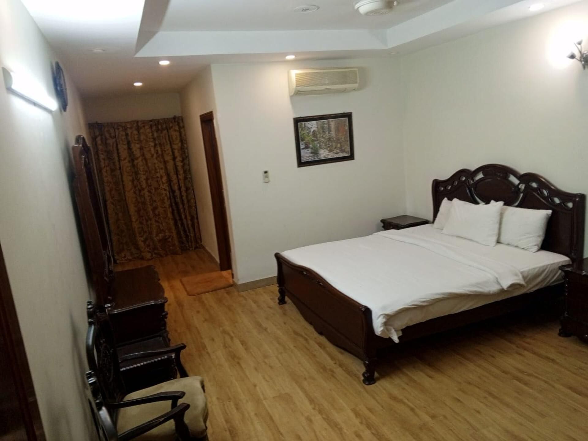 A bedroom with a wooden bed, a nightstand, a chair, and a door leading to another room.
