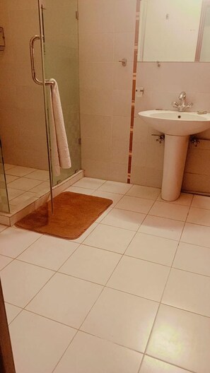 A bathroom with a glass shower enclosure, a white sink, and a brown bath mat.