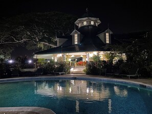Une vue nocturne d’un hôtel doté d’une piscine, d’un patio couvert et d’une tour surmontée d’un dôme.