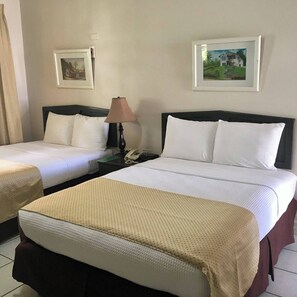 Une chambre d’hôtel avec deux lits, une table de chevet avec une lampe et deux tableaux encadrés au mur.