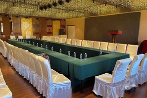 Un salón de conferencias con una larga mesa, sillas blancas y un mantel verde.