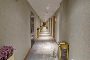 Un largo pasillo con alfombra estampada, puertas a ambos lados y una pequeña planta a la izquierda.