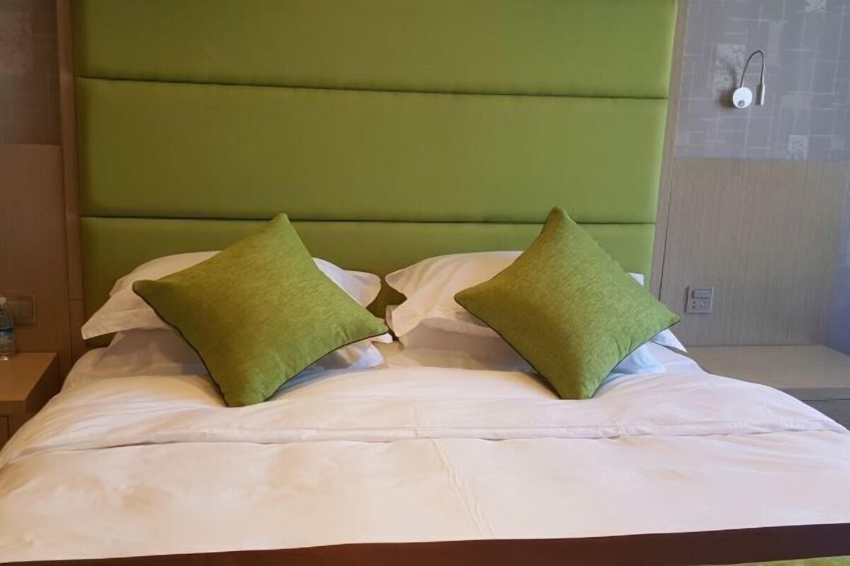 Cama com cabeceira estofada verde e duas almofadas verdes.