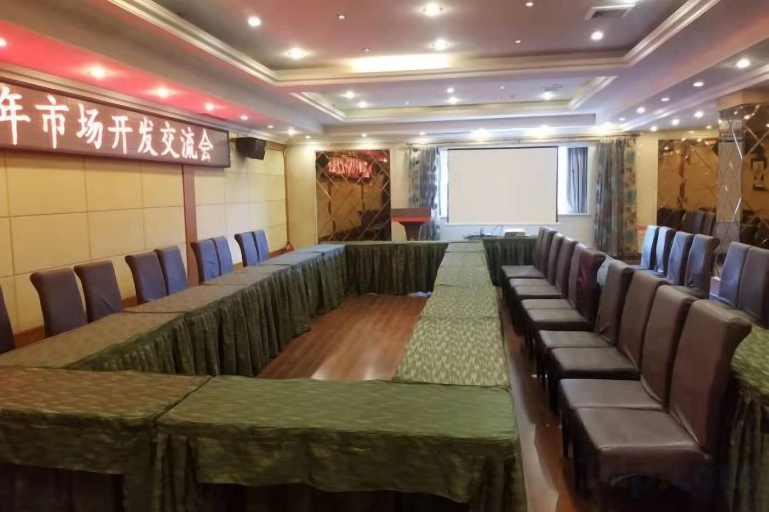 A conference room with a long table and chairs, a projector screen, and a banner on the wall.
