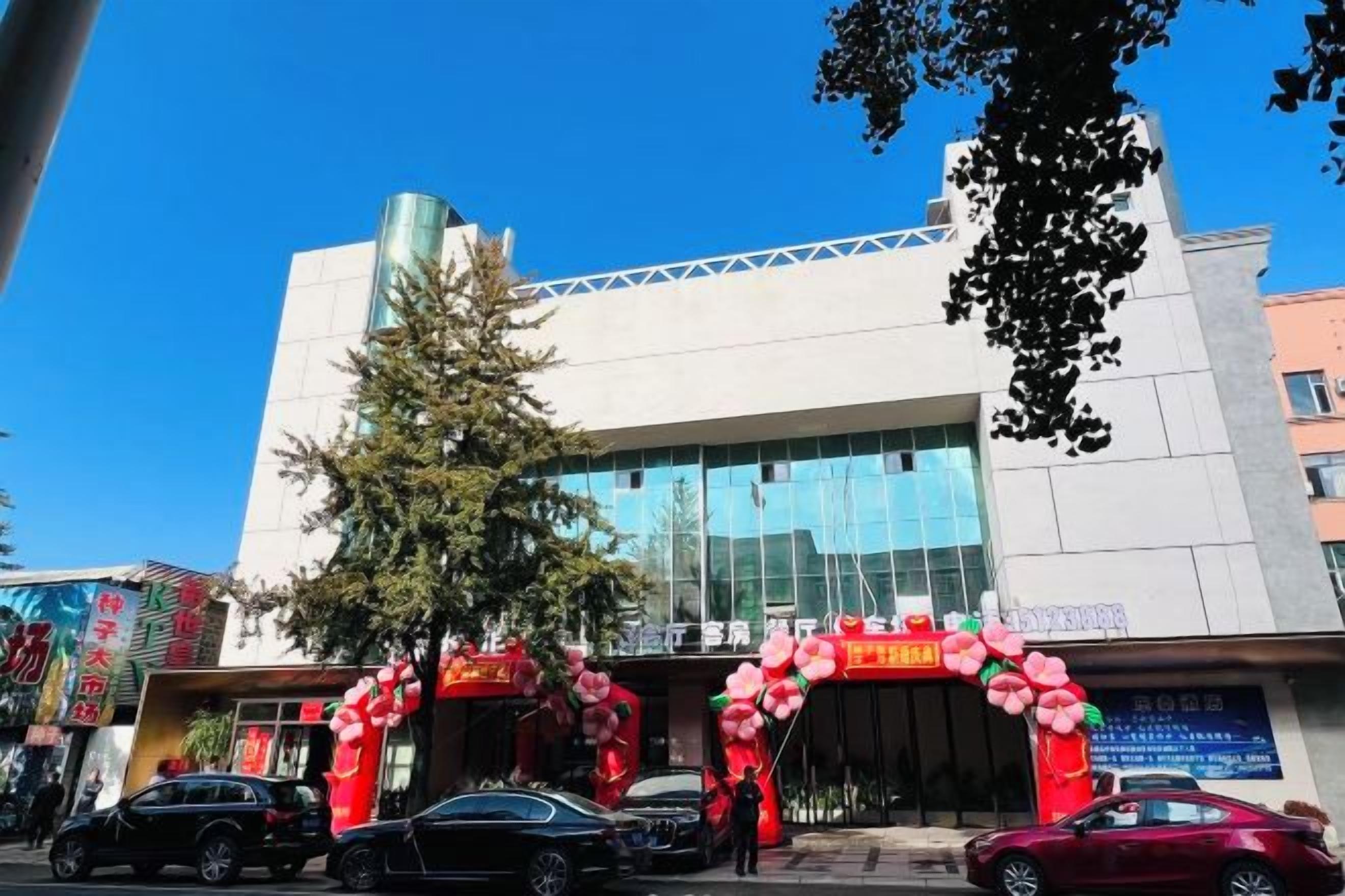 Un edificio con fachada moderna, amplios ventanales de vidrio y una entrada destacada decorada con rojo y blanco.