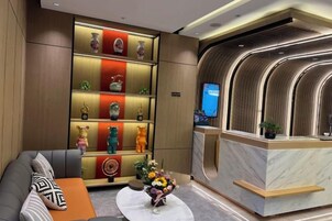 Zona de recepción de un hotel con un sofá, una mesa de recepción y una pared con estantes que exhiben diversos objetos decorativos.