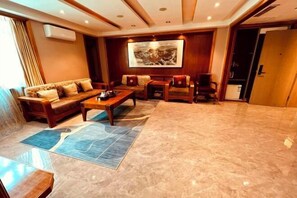 A spacious room with a large sofa set, a coffee table, and a dining table. There is a large framed artwork on the wall and a door leading to another area. - Dongtai Dashijie Hotel (Kuandian)