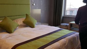 Ein Hotelzimmer mit Bett, grünem Kopfteil, Nachttisch und einem Vorhangfenster.