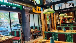 A restaurant interior with wooden tables and chairs, hanging green lamps, and a view of the street outside. - Dongtai Dashijie Hotel (Kuandian)