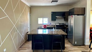Una cocina moderna con una isla central, armarios oscuros, electrodomésticos de acero inoxidable y una ventana que proporciona luz natural.
