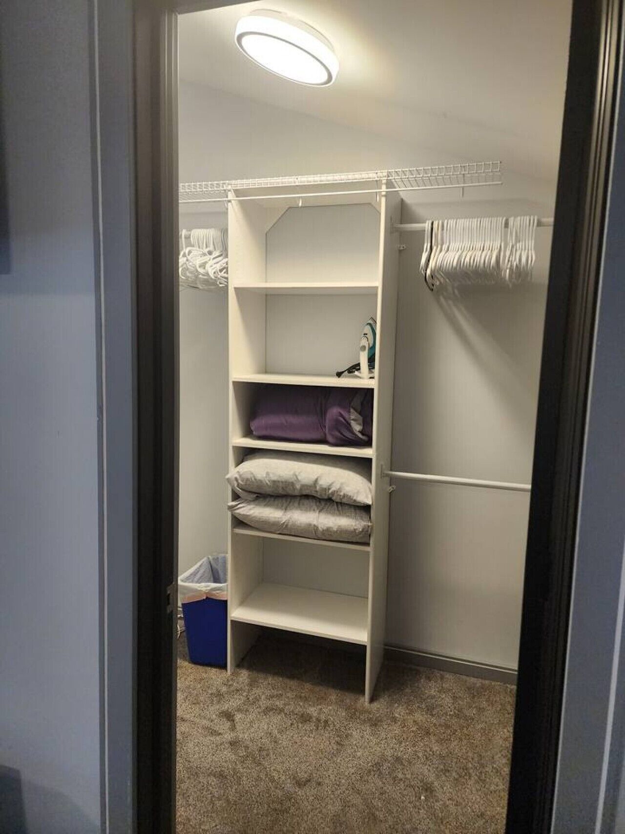 A walk-in closet with open shelves, a hanging rod, and a small ironing board.