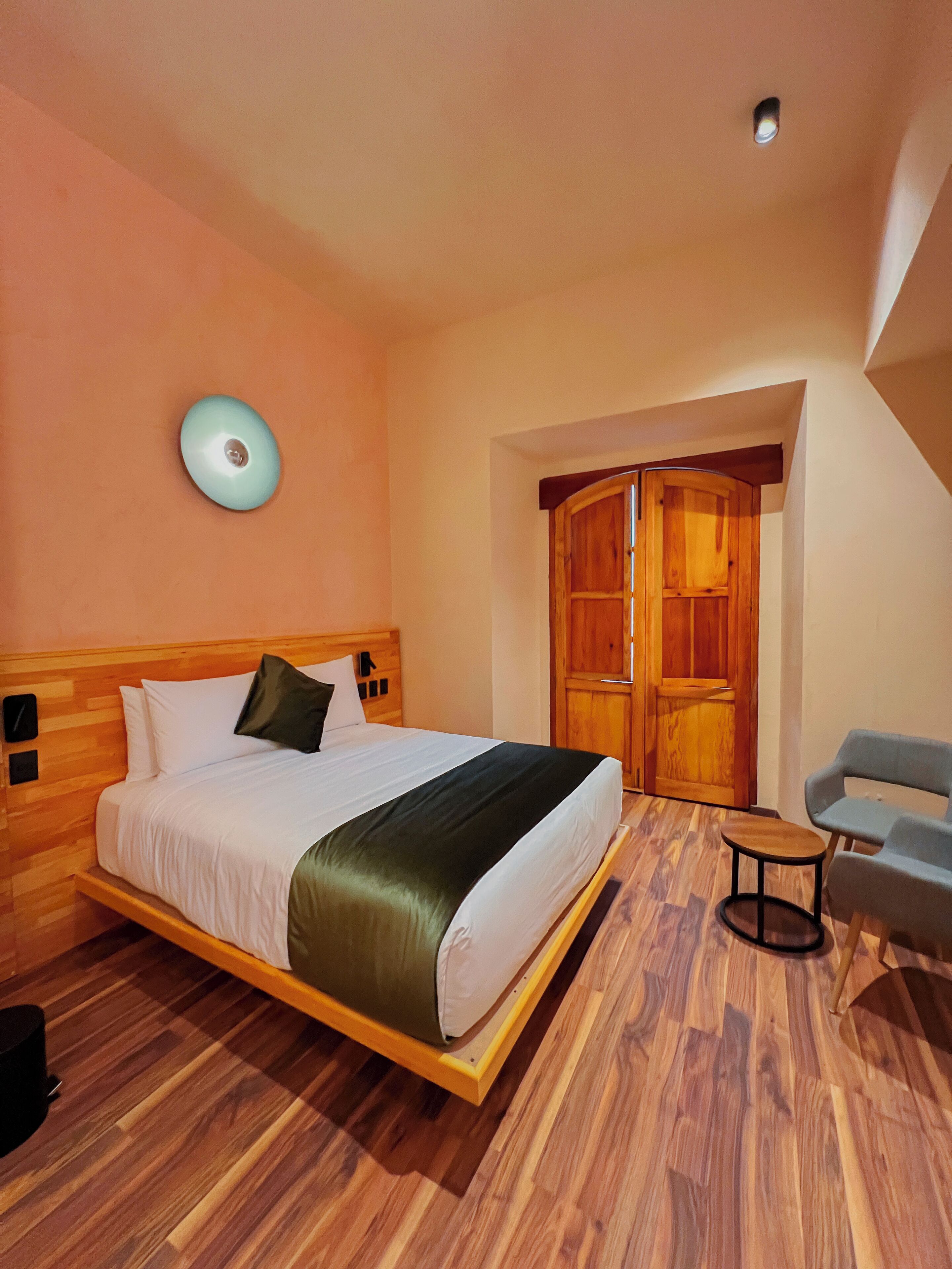 Un dormitorio con una cama de madera, una mesita redonda pequeña, una silla azul y un armario de madera.