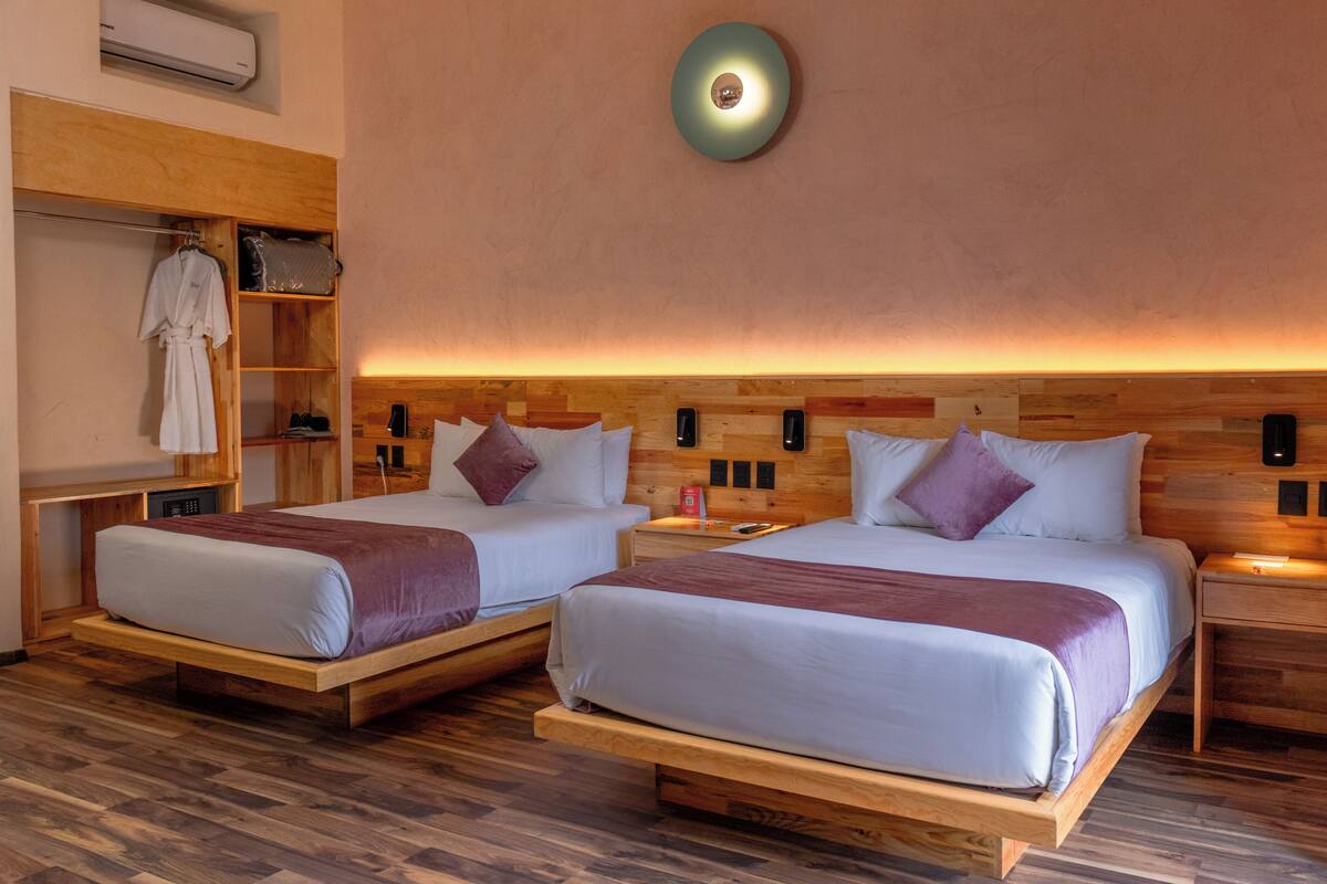 A hotel room with two beds, wooden headboards, a built-in wardrobe, and a wall-mounted light fixture.