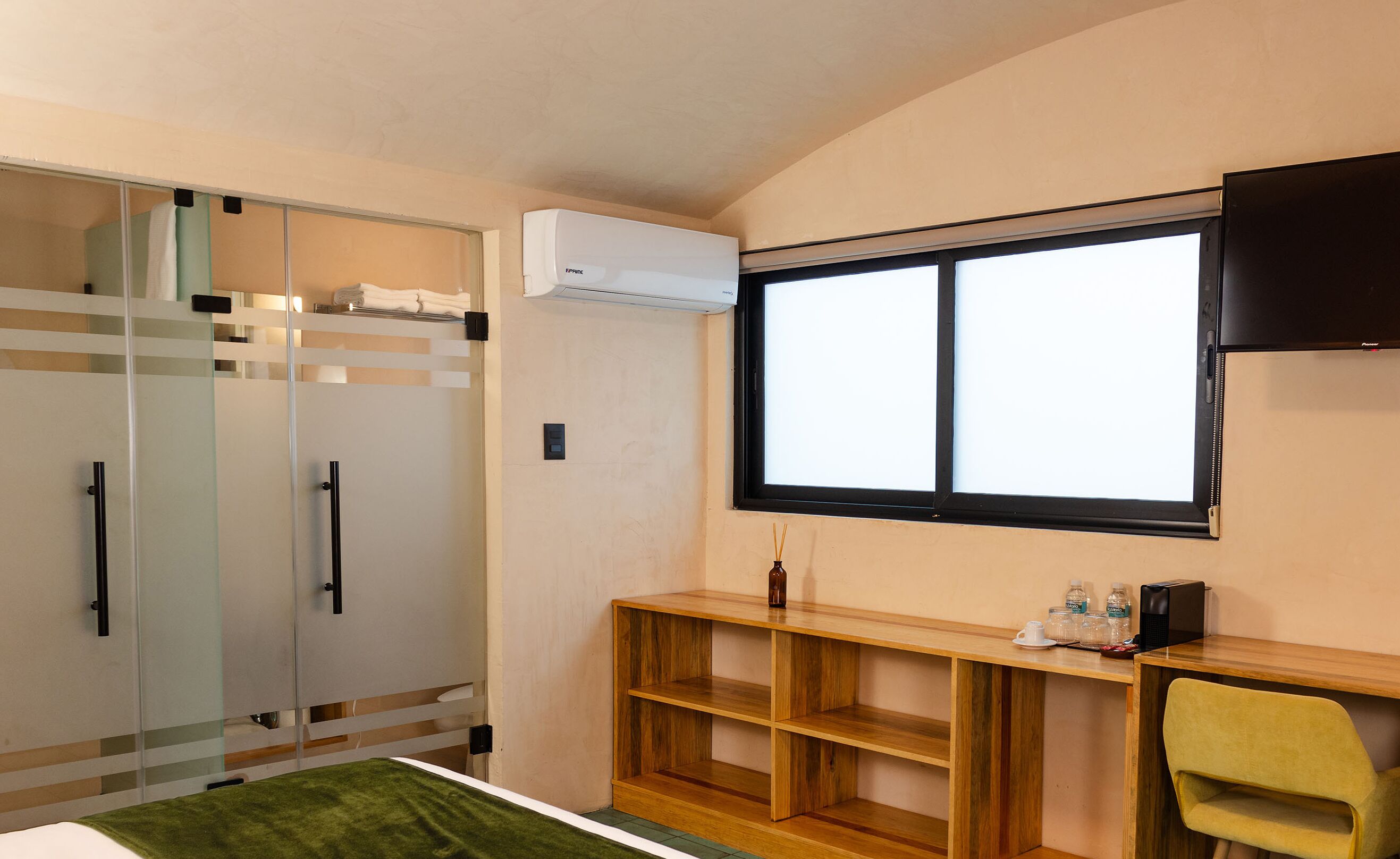 A hotel room with a bed, a wardrobe, a desk with a chair, a window, and an air conditioning unit.