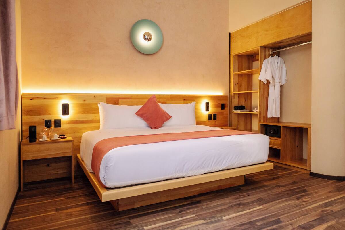 A modern hotel room with a wooden bed, a nightstand, a built-in wardrobe, and a wall-mounted light fixture.
