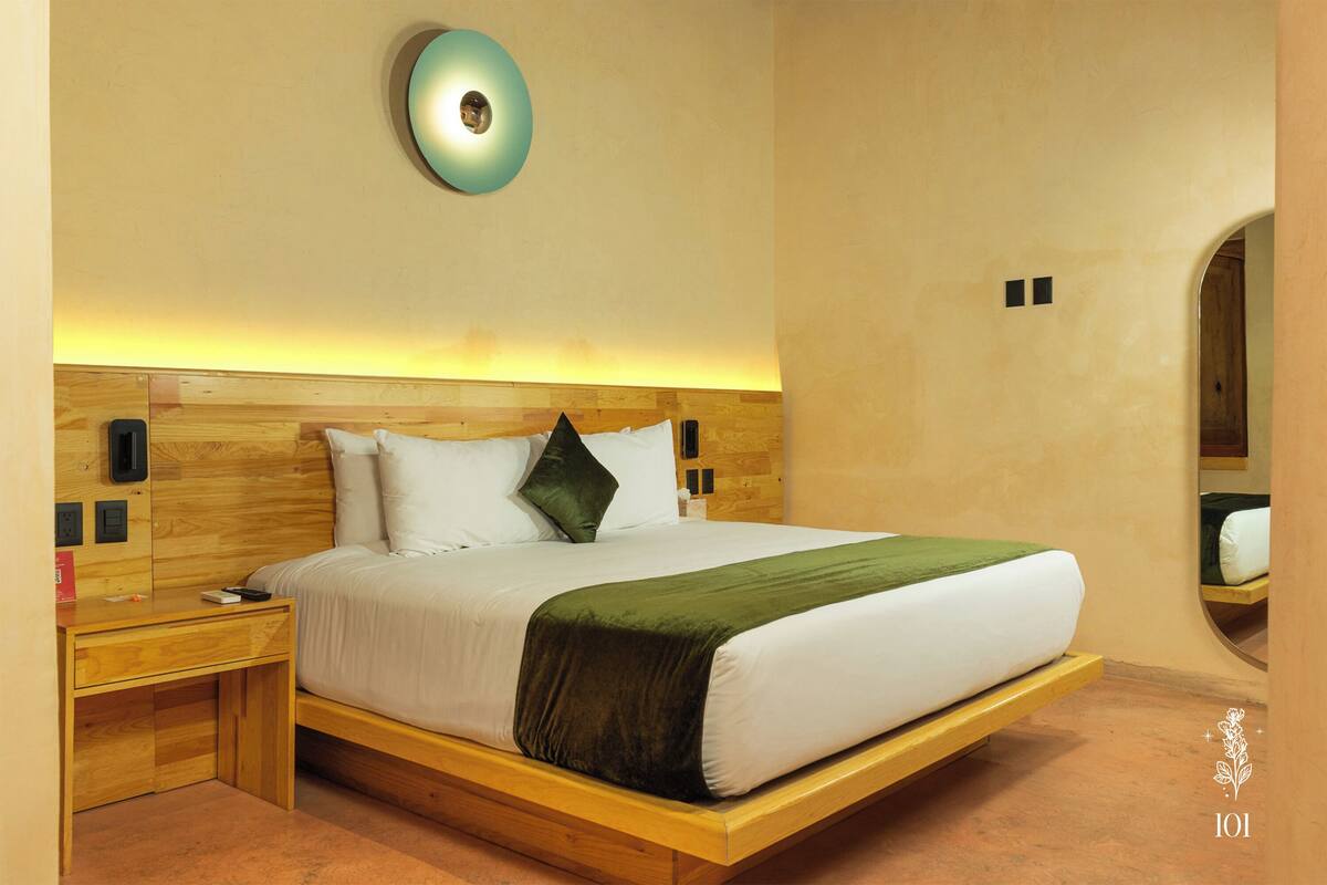 A modern hotel room with a wooden bed, a bedside table, and a wall-mounted light fixture.