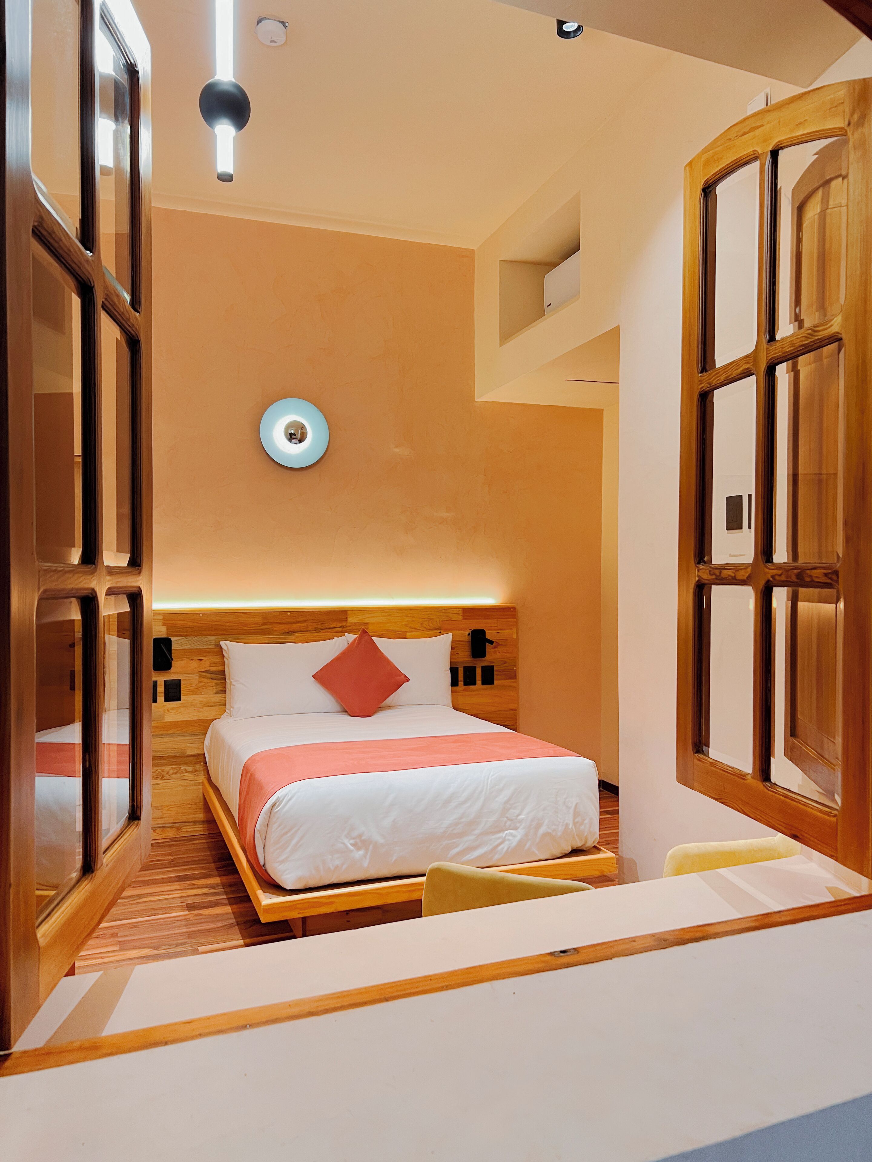 Une chambre d’hôtel compacte comprenant un lit, une tête de lit en bois et des étagères intégrées.