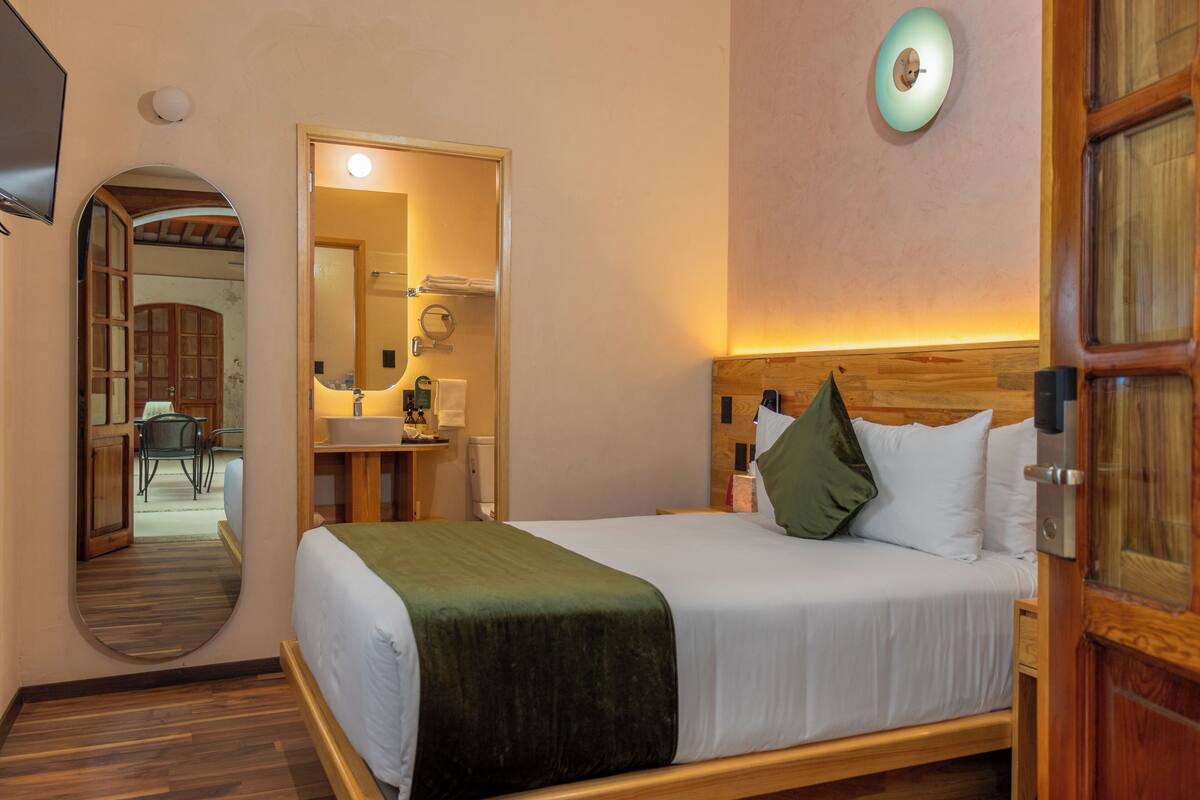 A hotel room with a bed, a wooden headboard, a mirror, and a wooden door.