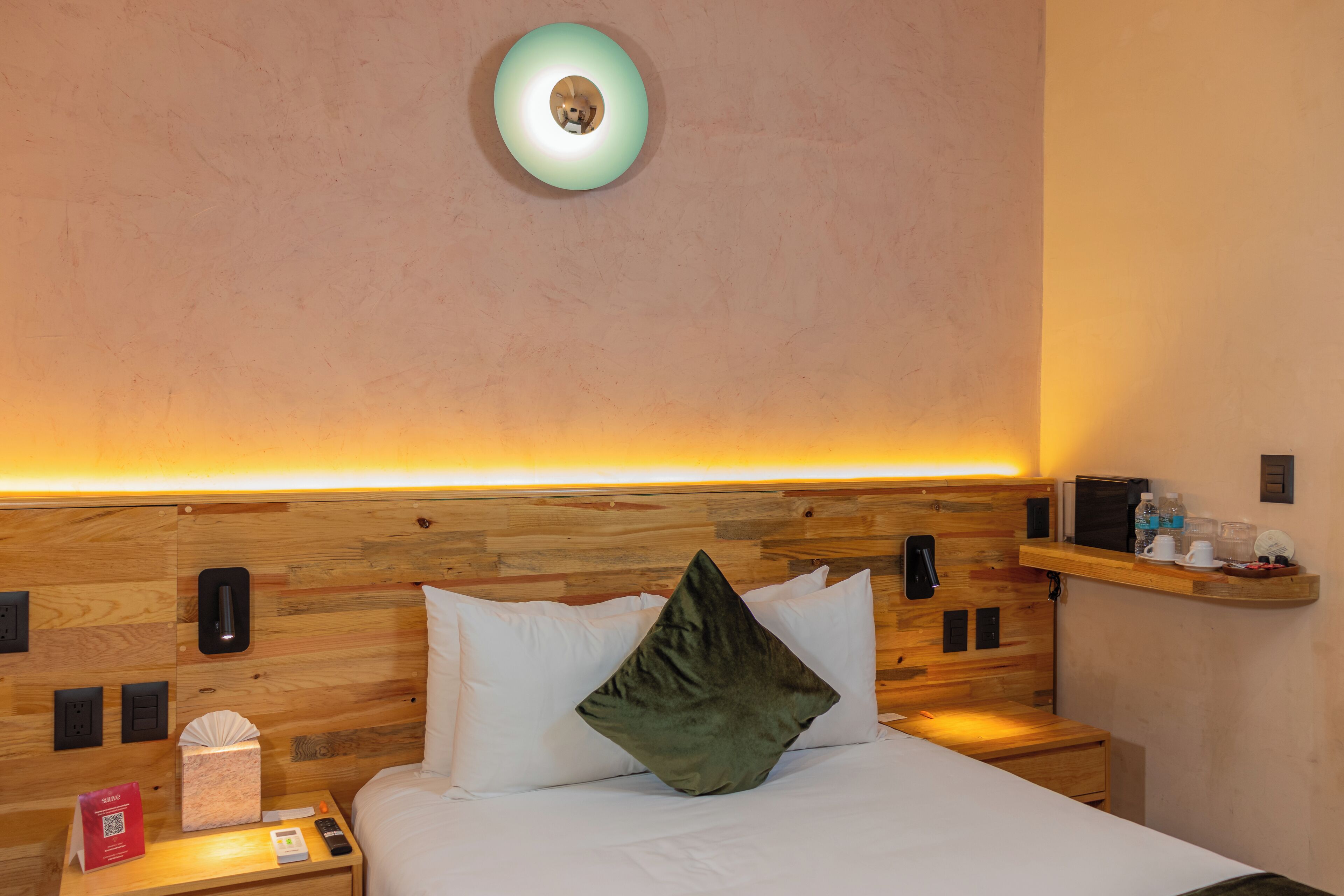 A hotel room with a wooden headboard, a bedside table with a tissue box, a phone, and a bedside lamp.