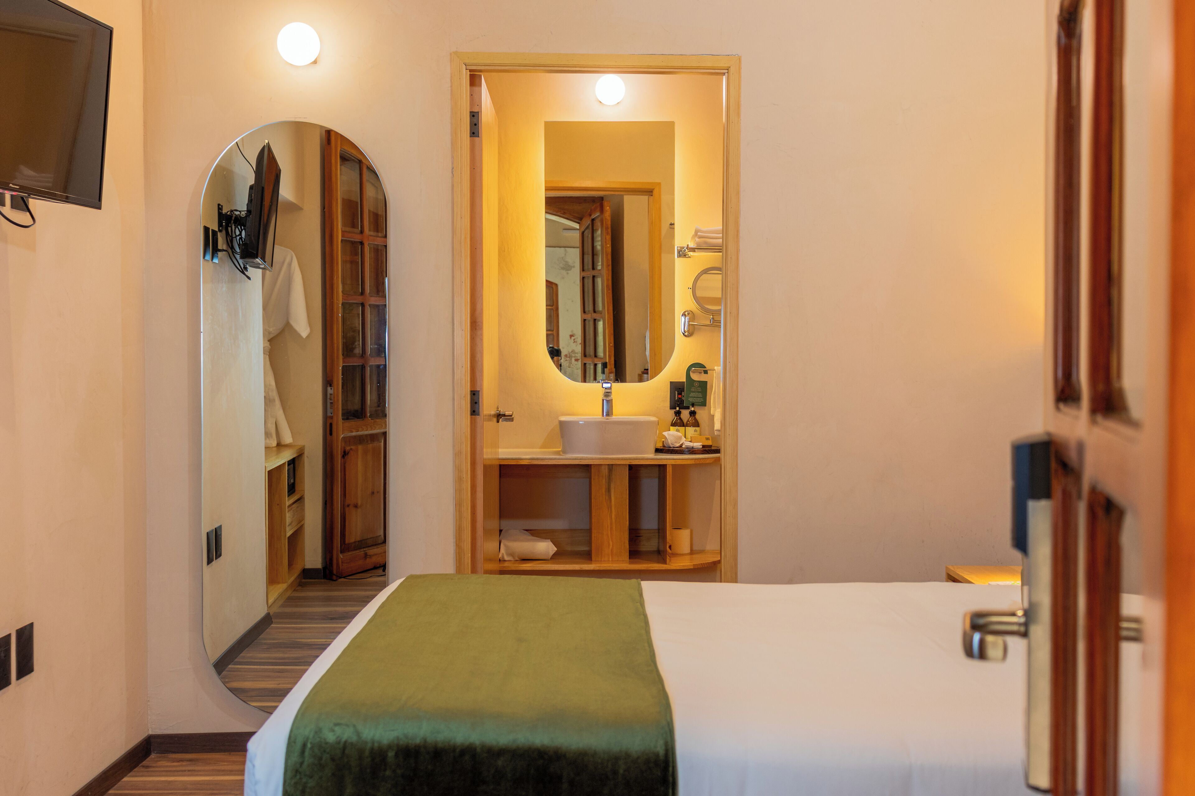 A hotel room with a bed, a mirror, a sink, and a wooden cabinet.