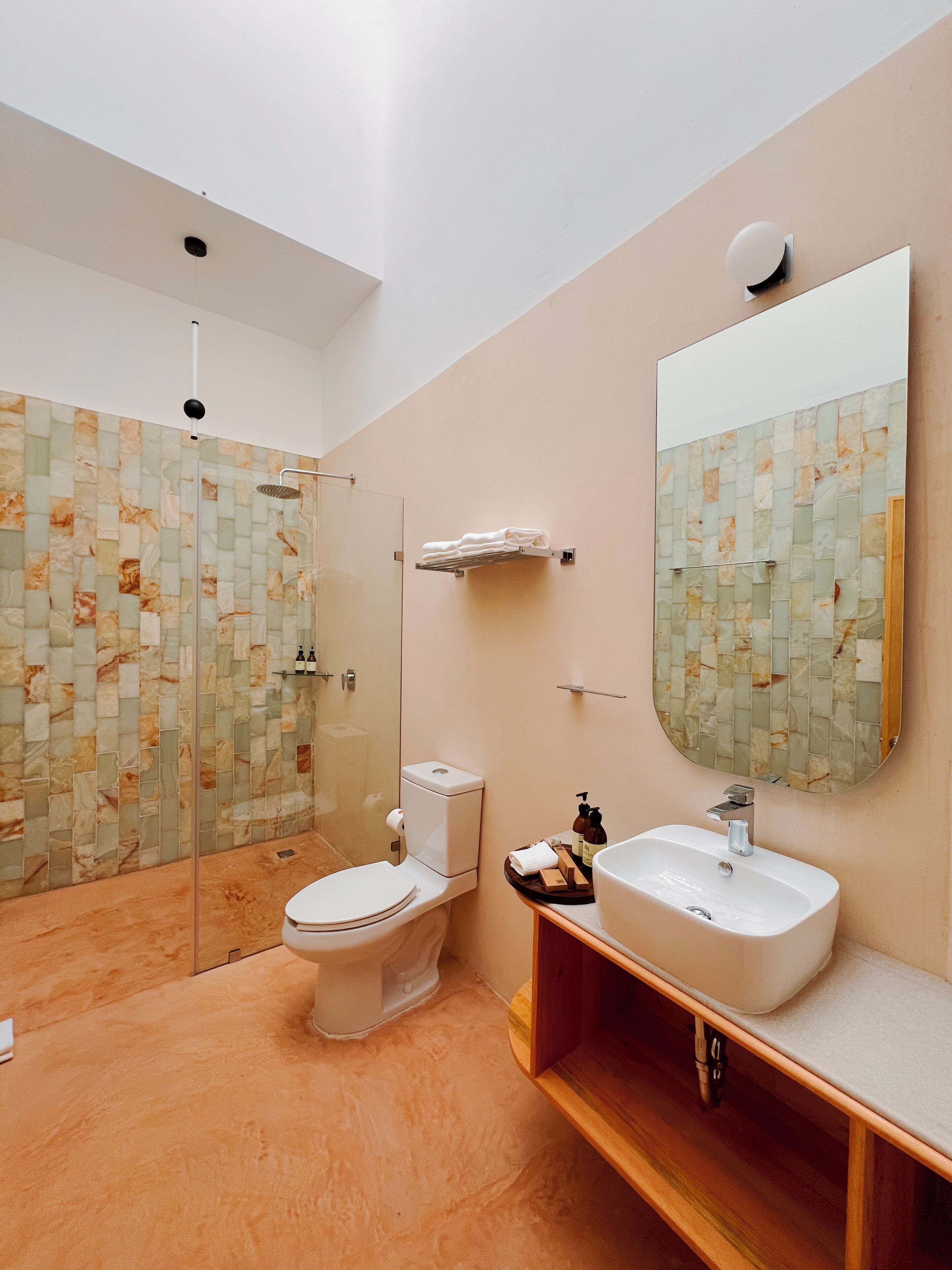A modern bathroom with a glass-enclosed shower, a toilet, a sink with a mirror, and a wooden vanity.