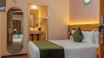 A hotel room with a wooden bed, a mirror, a desk with a chair, and a bathroom visible through an archway.
