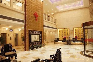 A hotel lobby with a reception desk, seating area, and a decorative wall.