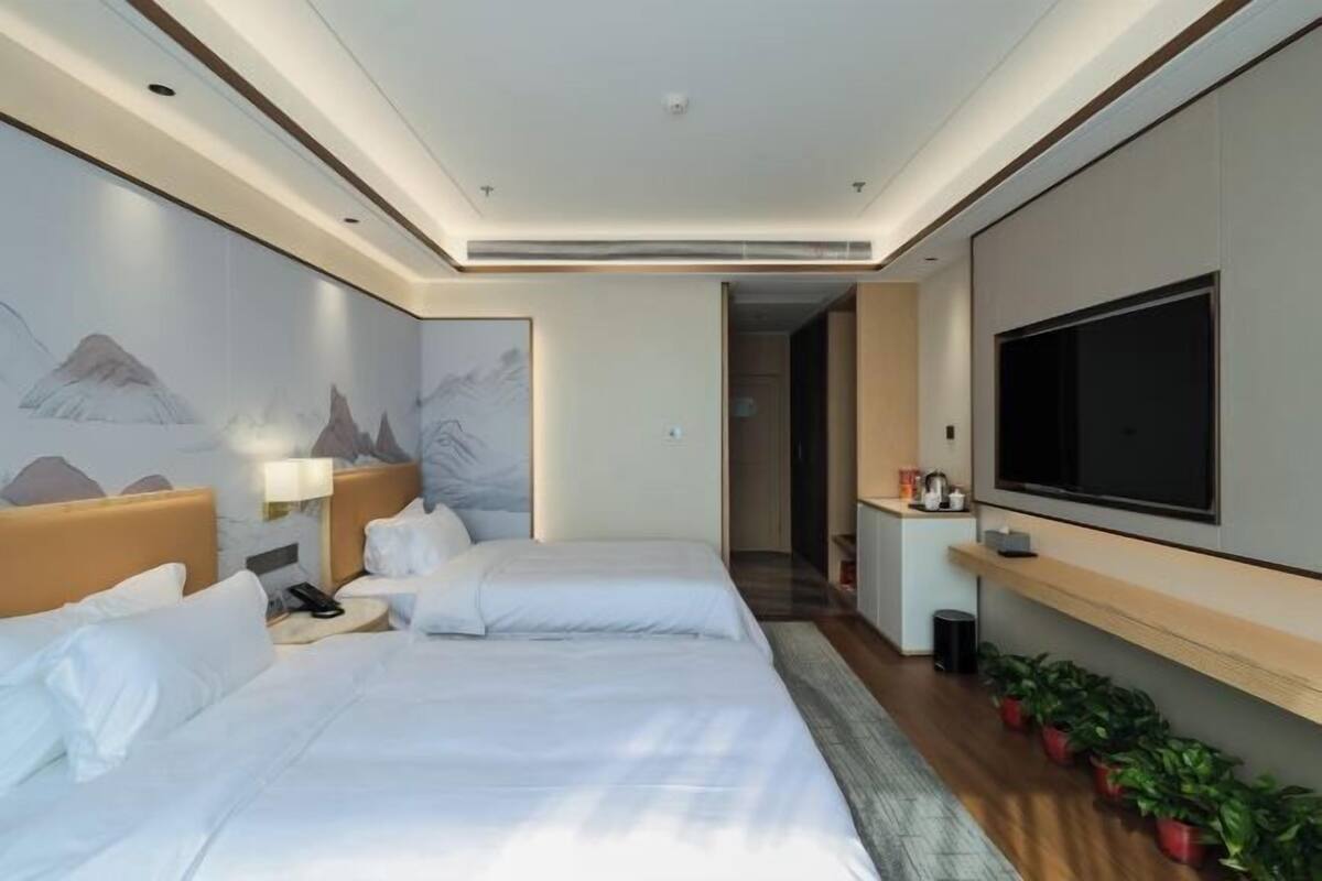A hotel room with two beds, a TV, a desk, and a wall-mounted TV.