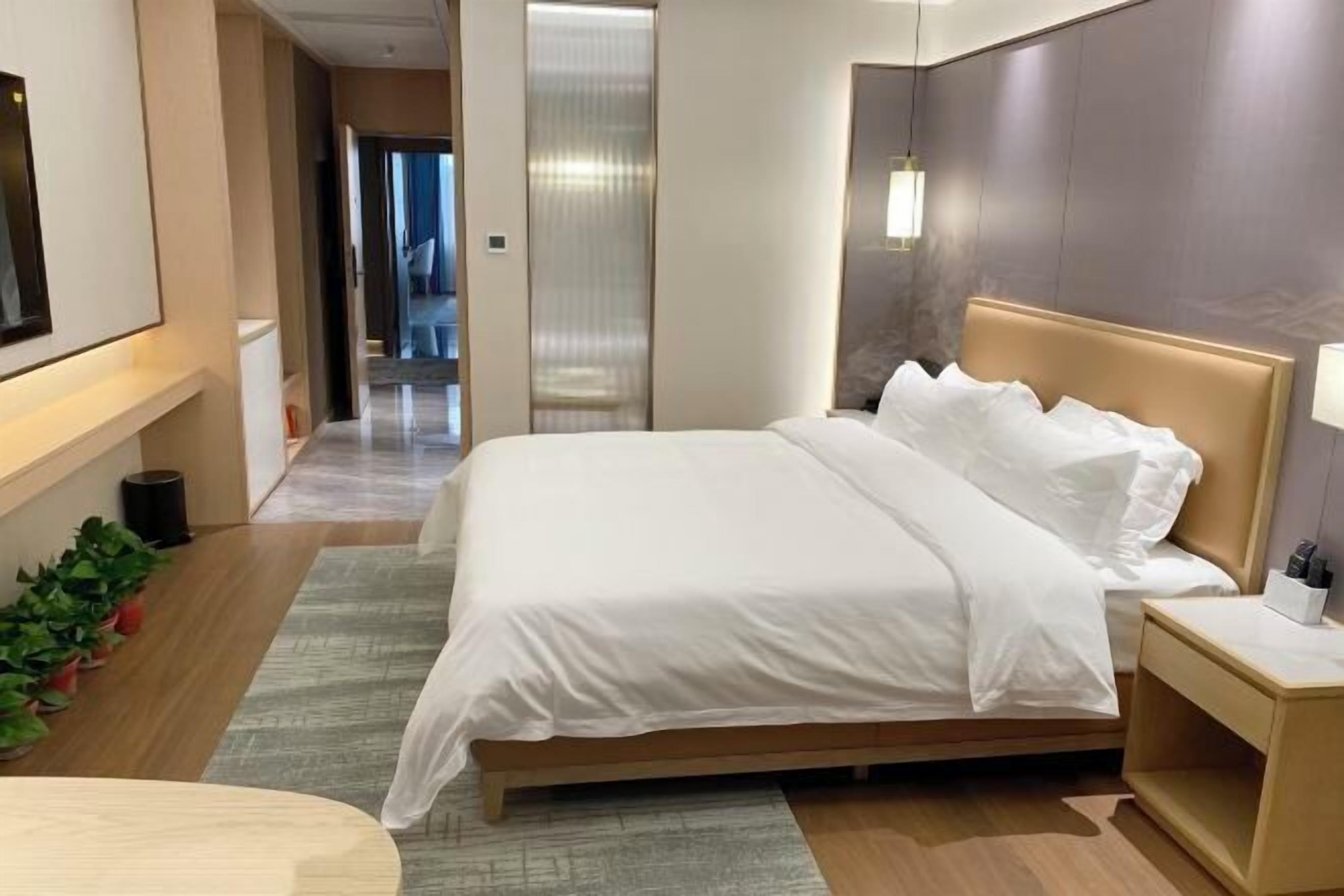 Habitación de hotel con una cama grande, una mesita de noche, una lámpara y vistas al pasillo.