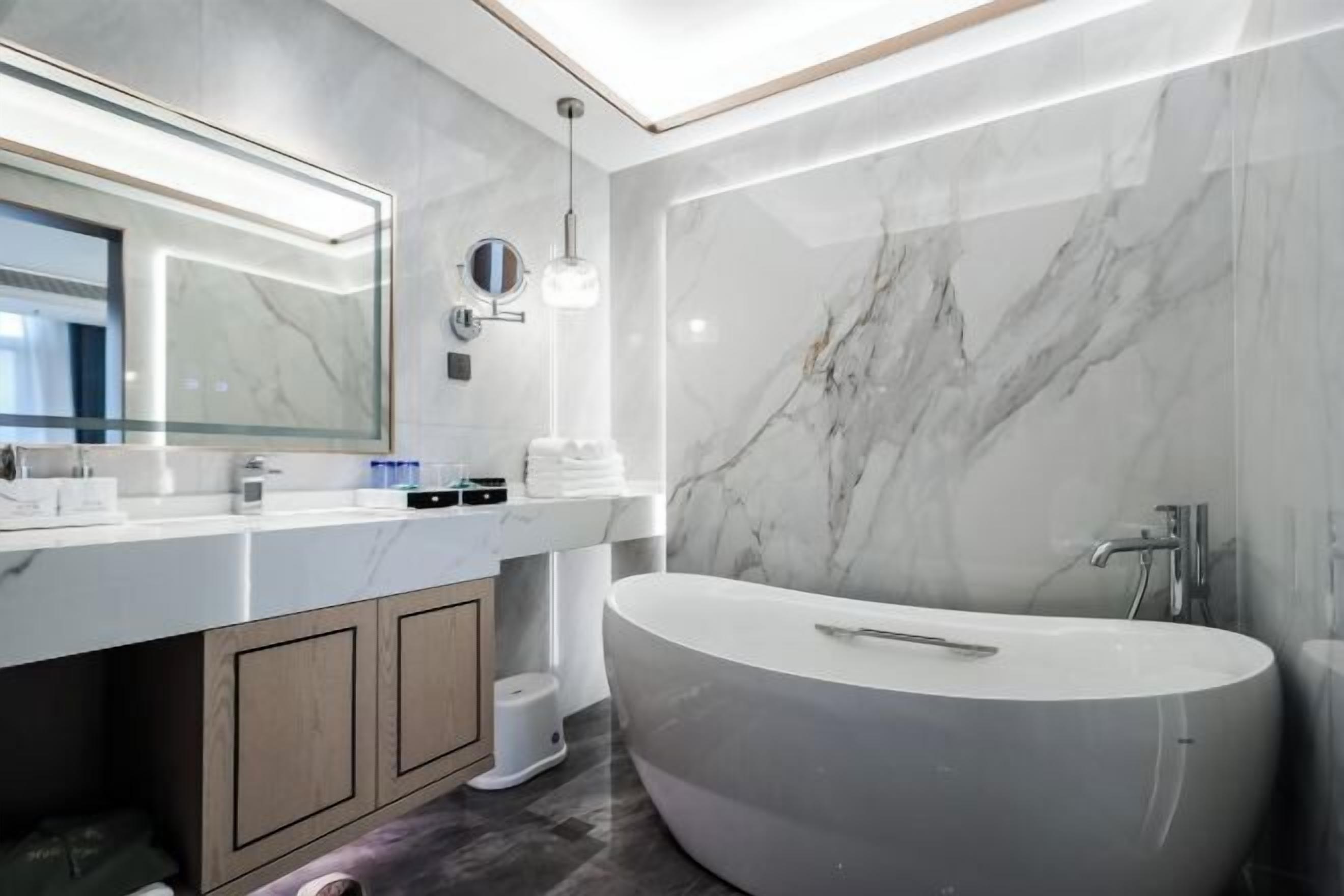A modern bathroom with a large freestanding bathtub, a vanity with a mirror, and marble walls.