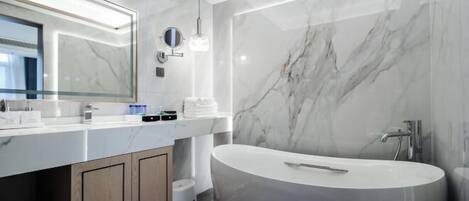 A modern bathroom with a large freestanding bathtub, a vanity with a mirror, and marble walls.
