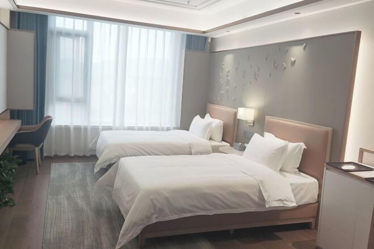 Una habitación de hotel con dos camas, un escritorio y un ventanal con cortinas.