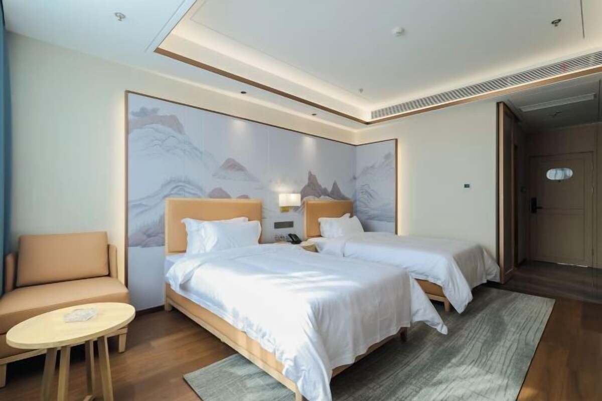 Habitación de hotel con dos camas, un sofá, una mesita redonda y un mural grande en la pared.