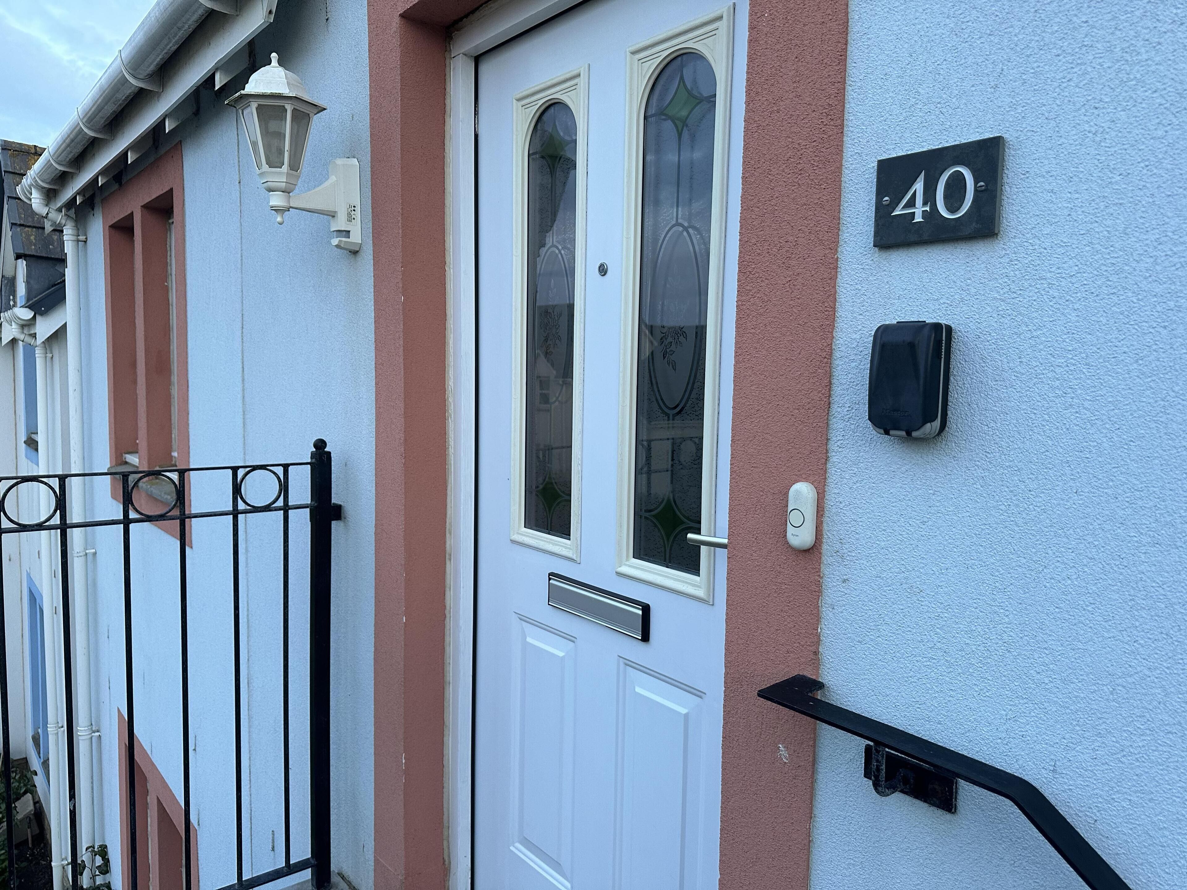Une porte blanche avec un panneau de verre, une boîte aux lettres noire et le numéro de la maison, « 40 », peint sur le mur.